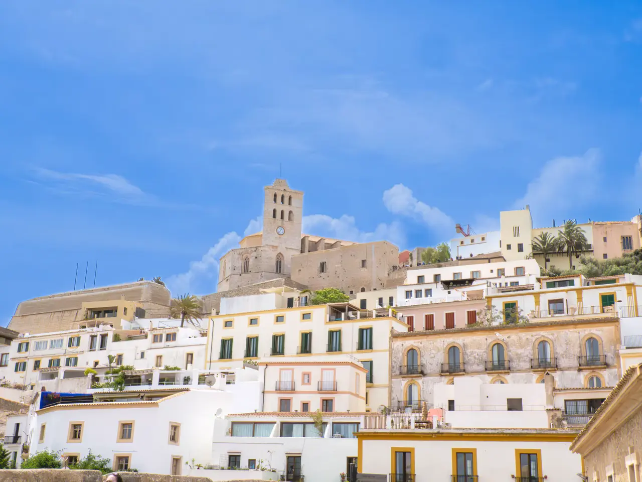 The cathedral bell tower rising above whitewashed Dalt Vila houses with yellow-trimmed windows under a bright blue sky