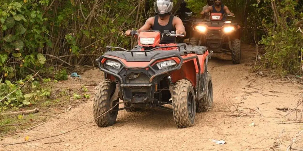 Two riders in helmets on red ATVs on a dirt track under trees