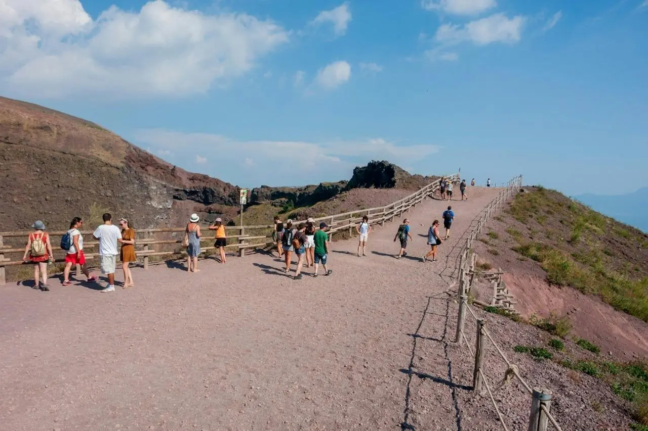 Walkers on the gravel path along the crater rim of Mount Vesuvius under a blue sky