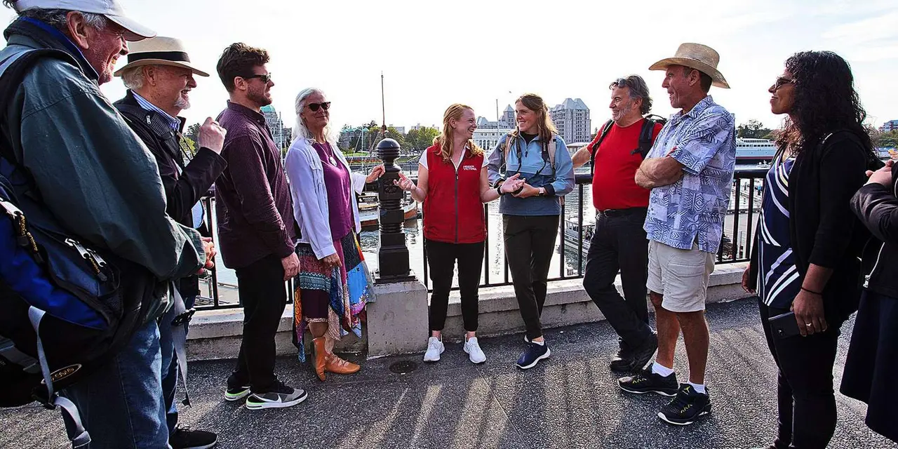 A guide in a red vest talking to a small group on Victoria's harbour walkway